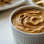 How to Make Velvety Chipotle Queso Like a Pro 13 A creamy, smoky chipotle queso dip in a white bowl, garnished with flecks of chipotle peppers and served with crispy tortilla chips.